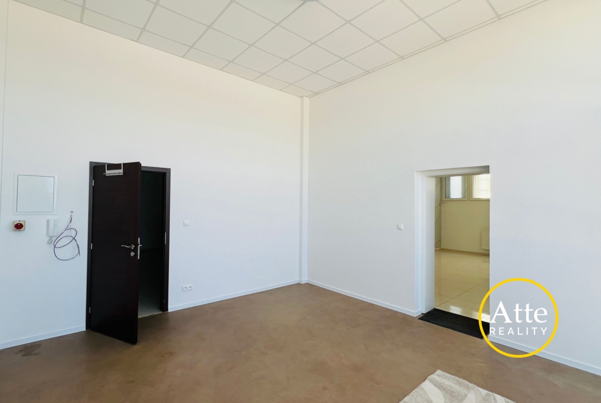 Empty office-like room with white walls, brown floor, a dark open door on the left, and a doorway to another room on the right.