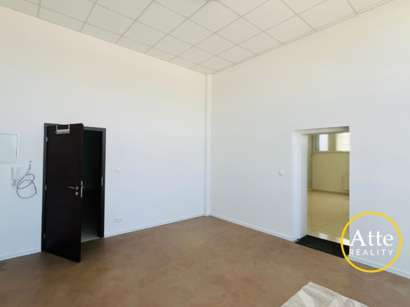 Empty office-like room with white walls, brown floor, a dark open door on the left, and a doorway to another room on the right.