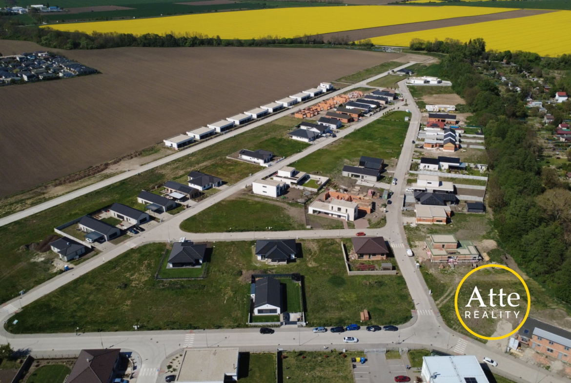 Aerial view of a new suburban neighborhood with rows of houses along streets, brown fields nearby and a bright yellow crop field in the distance.