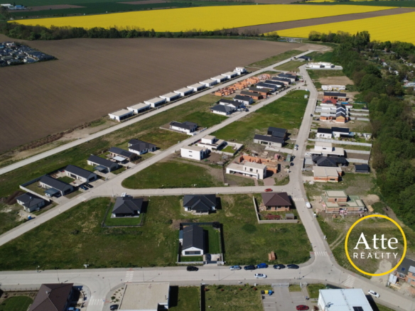 Aerial view of a new suburban neighborhood with rows of houses along streets, brown fields nearby and a bright yellow crop field in the distance.