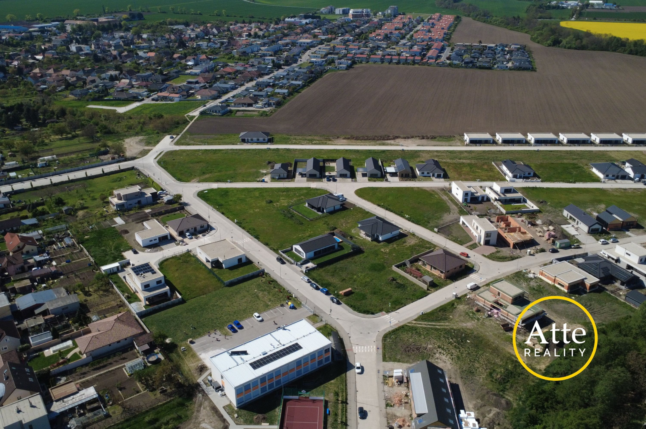 Aerial view of a suburban development with rows of new houses, roads, and surrounding fields.