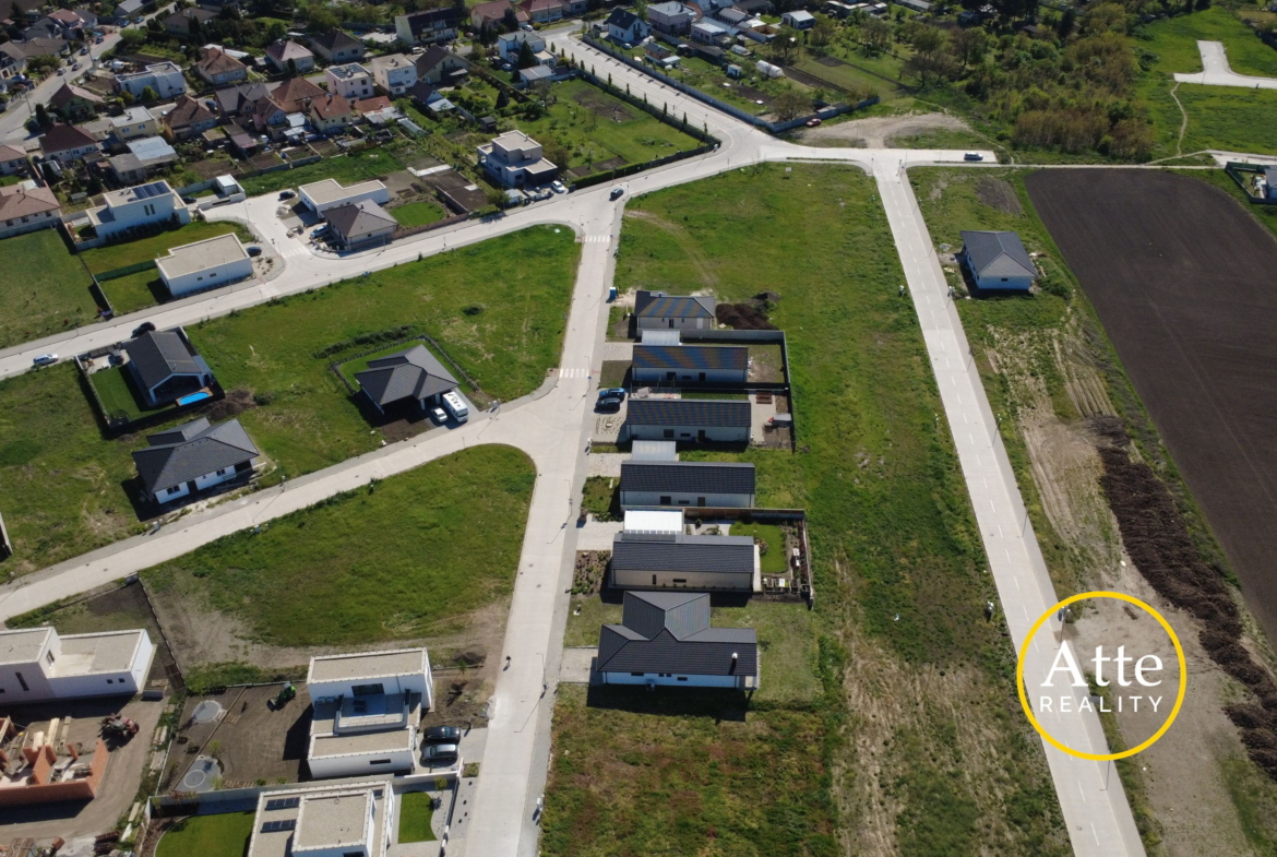 Aerial view of a suburban neighborhood with intersecting roads, rows of houses and gardens, and a large plowed field on the right; watermark reads Arte Realty.