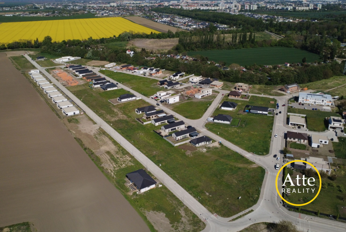 Aerial view of a suburban housing development along curving streets beside a bright yellow canola field and green farmland.