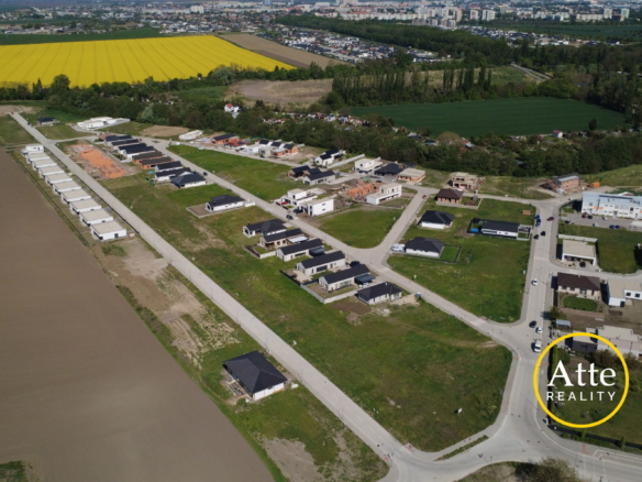 Aerial view of a suburban housing development along curving streets beside a bright yellow canola field and green farmland.
