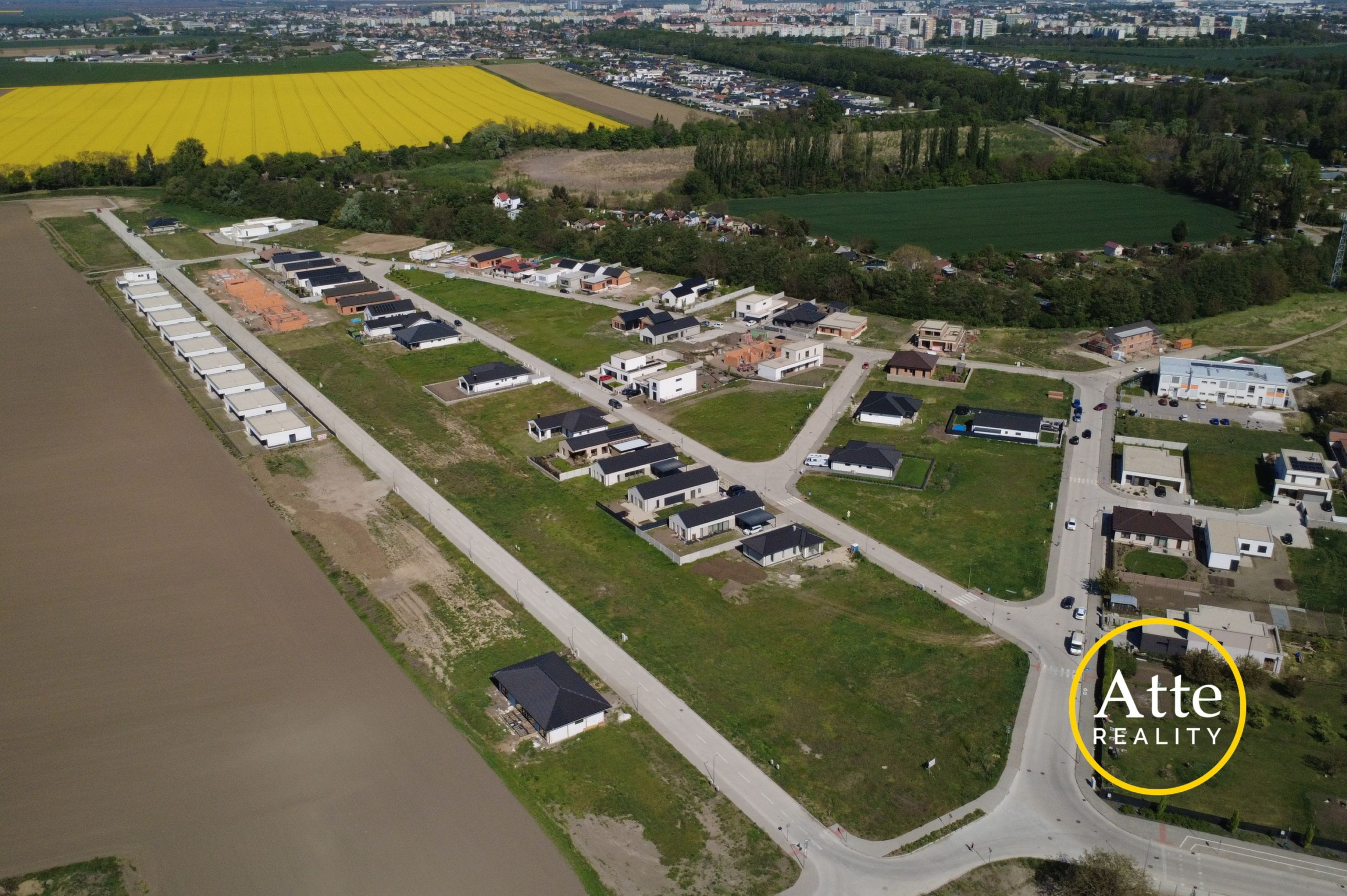 Aerial view of a suburban housing development along curving streets beside a bright yellow canola field and green farmland.