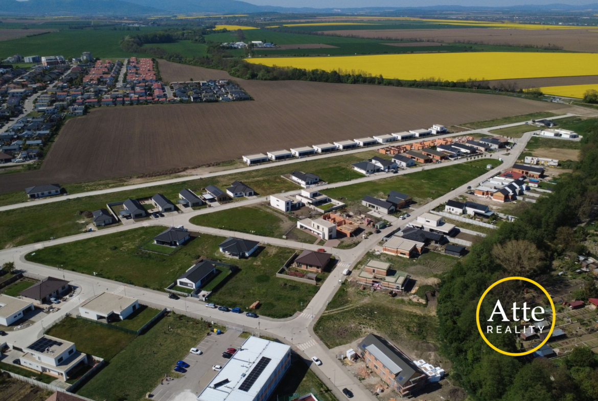 Aerial view of a developing suburban neighborhood bordered by empty brown fields and bright yellow canola fields in the distance.