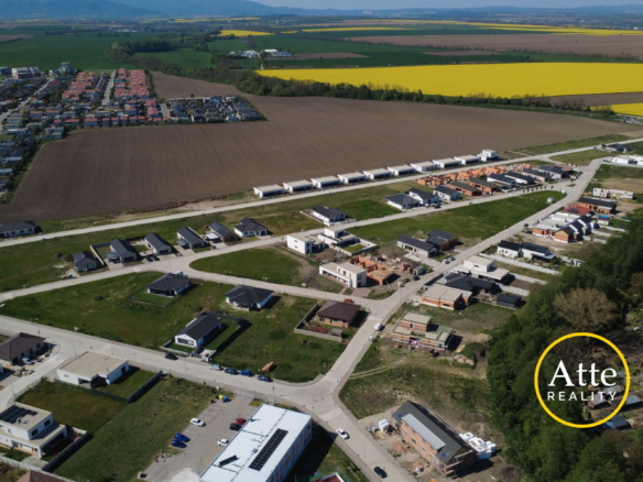 Aerial view of a developing suburban neighborhood bordered by empty brown fields and bright yellow canola fields in the distance.