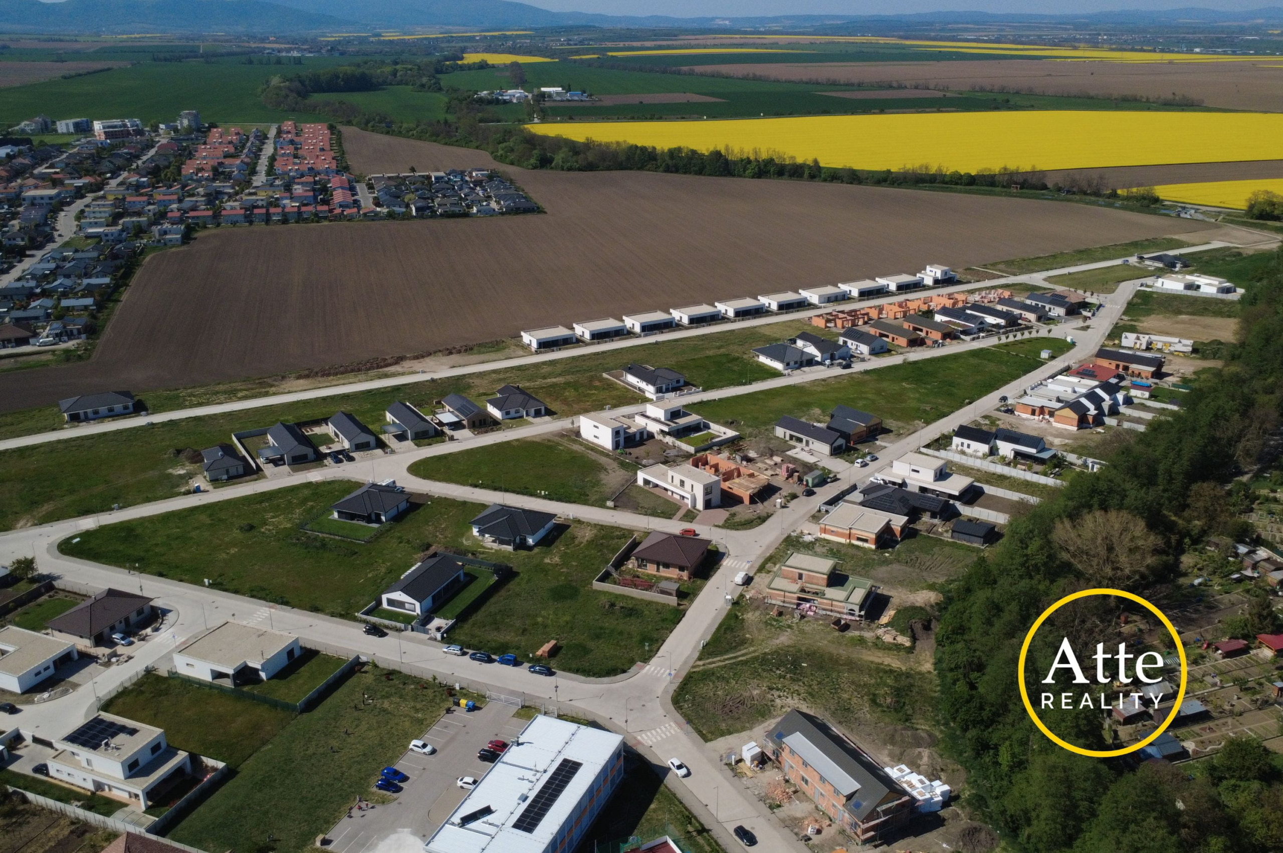 Aerial view of a developing suburban neighborhood bordered by empty brown fields and bright yellow canola fields in the distance.